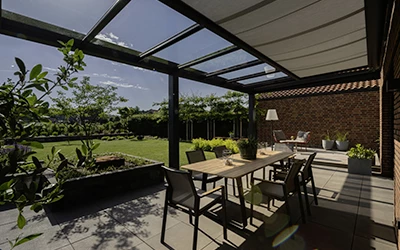 Überdachte Terrasse mit Markise, von innen fotografiert, Gartenmöbel und Pflanzen an einem sonnigen Tag